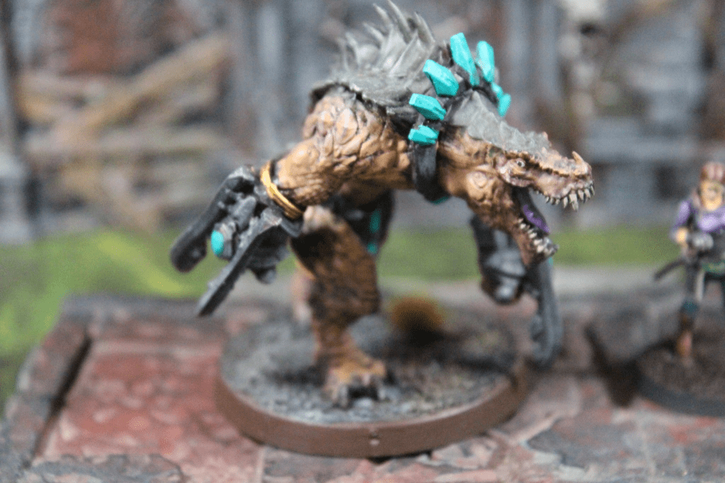 A detailed miniature of a monstrous creature with spiked armor and a mechanical arm, standing on a textured base, alongside a female character in a fantasy setting.