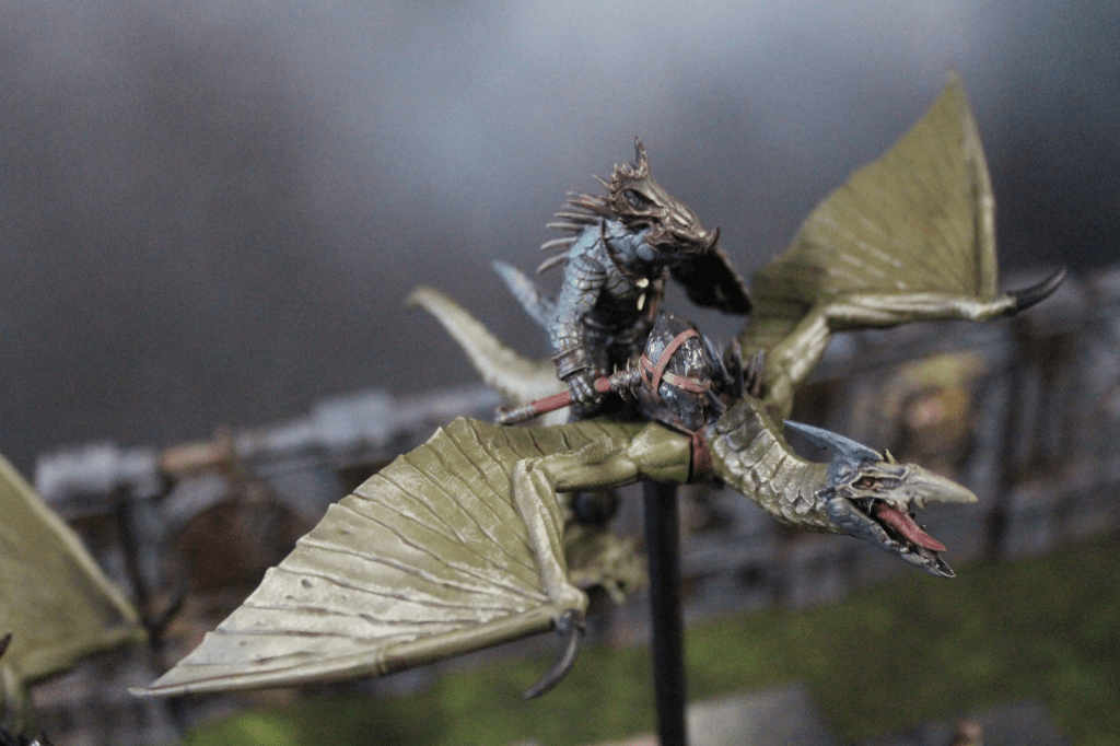 A close-up of a detailed tabletop miniature featuring a humanoid figure riding a large, winged creature, set against a blurred background.