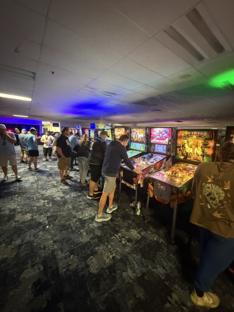 A vibrant arcade filled with people playing pinball machines, featuring colorful artwork and illuminated displays.
