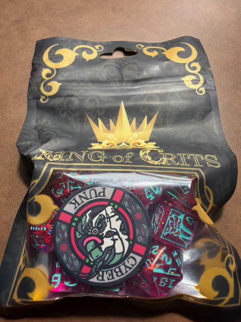 A package of gaming dice labeled 'King of Crits' featuring colorful designs and a circular token with a graphic in the center.