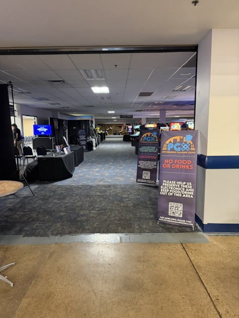 View of an event hall entrance with tables, gaming machines, and signs indicating no food or drinks allowed.