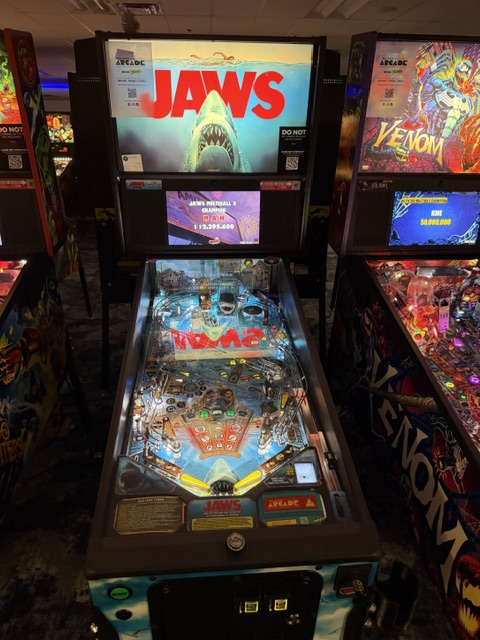 Pinball machine themed after the movie Jaws, featuring a colorful playfield with shark imagery and bright lighting.