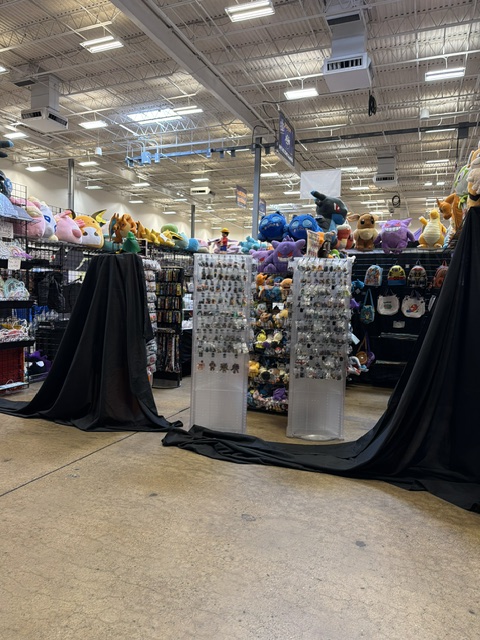 Indoor retail space featuring displays of plush toys and accessories, with black drapes hanging in the foreground.