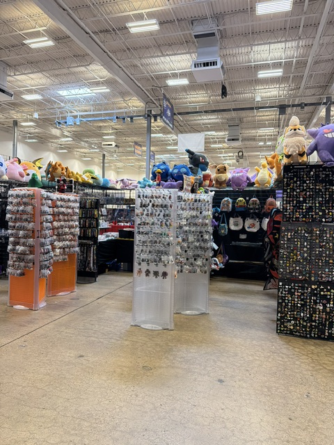 A retail store interior showcasing various merchandise, including plush toys on tall shelves, accessory displays with pins and keychains, and colorful hats hanging in the background.