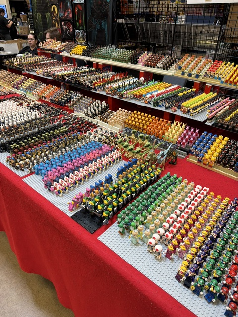 A vibrant display of various collectible figurines arranged in neat rows across tables covered with a red cloth, featuring a wide range of colors and designs.