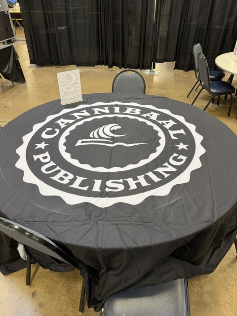 A round table covered with a black tablecloth featuring the logo of Cannibaal Publishing in white, displayed at an event.