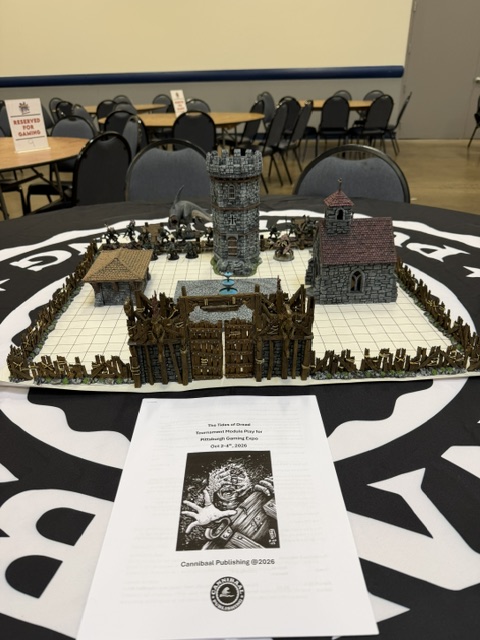 A detailed tabletop gaming setup featuring miniature buildings, a castle tower, and a fenced area, with a printed game rule booklet in front, all placed on a patterned tablecloth.