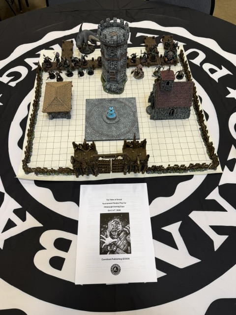A tabletop game setup featuring a miniature castle, buildings, and terrain elements, surrounded by a grid pattern on a black tablecloth. A printed game sheet is placed in the foreground, detailing game instructions.