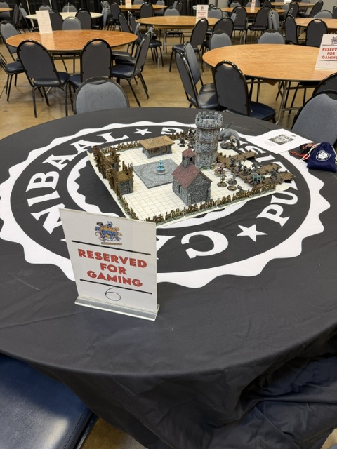A tabletop gaming setup featuring a detailed miniature scene with structures and characters on a table marked 'Reserved for Gaming'.