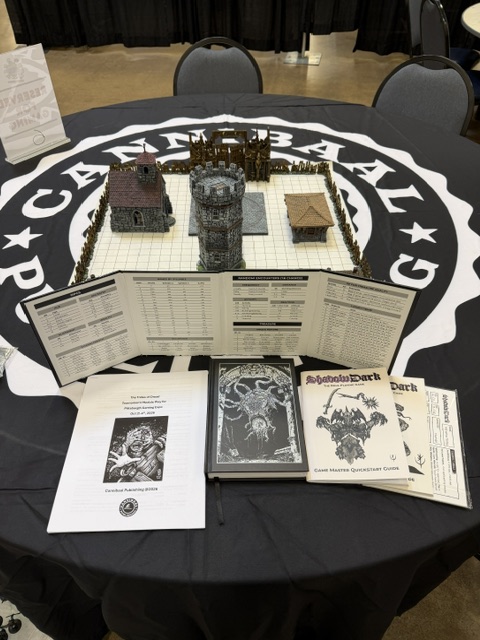 A tabletop gaming setup featuring a grid map with miniature buildings, a tower, and a wooden fence, surrounded by game master guides and rulebooks on a round table with a logo.