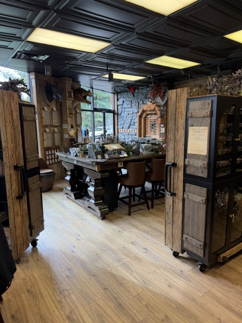 Interior view of a rustic-themed room featuring wooden doors, a large table with chairs, and decorative stone walls, with shelves displaying various items.