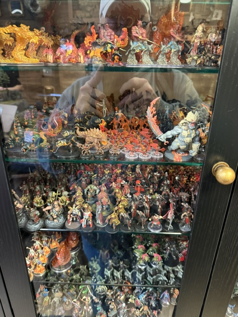 A display cabinet filled with a variety of detailed miniature figures, including fantasy characters, creatures, and colorful decorations.
