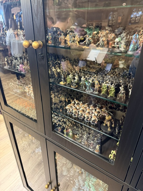 A glass display cabinet filled with numerous collectible figurines and miniature statues, showcasing a variety of characters and designs.