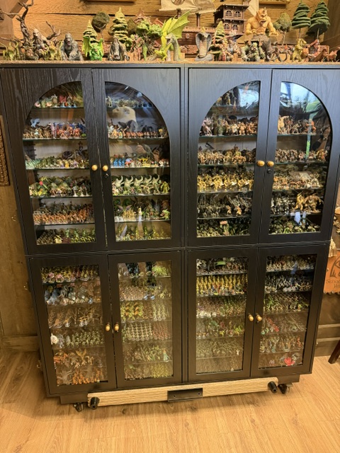 A black display cabinet filled with various figurines, including animals and fantasy characters, arranged neatly behind glass doors.