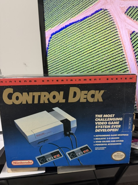 A boxed Nintendo Entertainment System Control Deck featuring graphics and descriptions highlighting its capabilities, including two controllers.